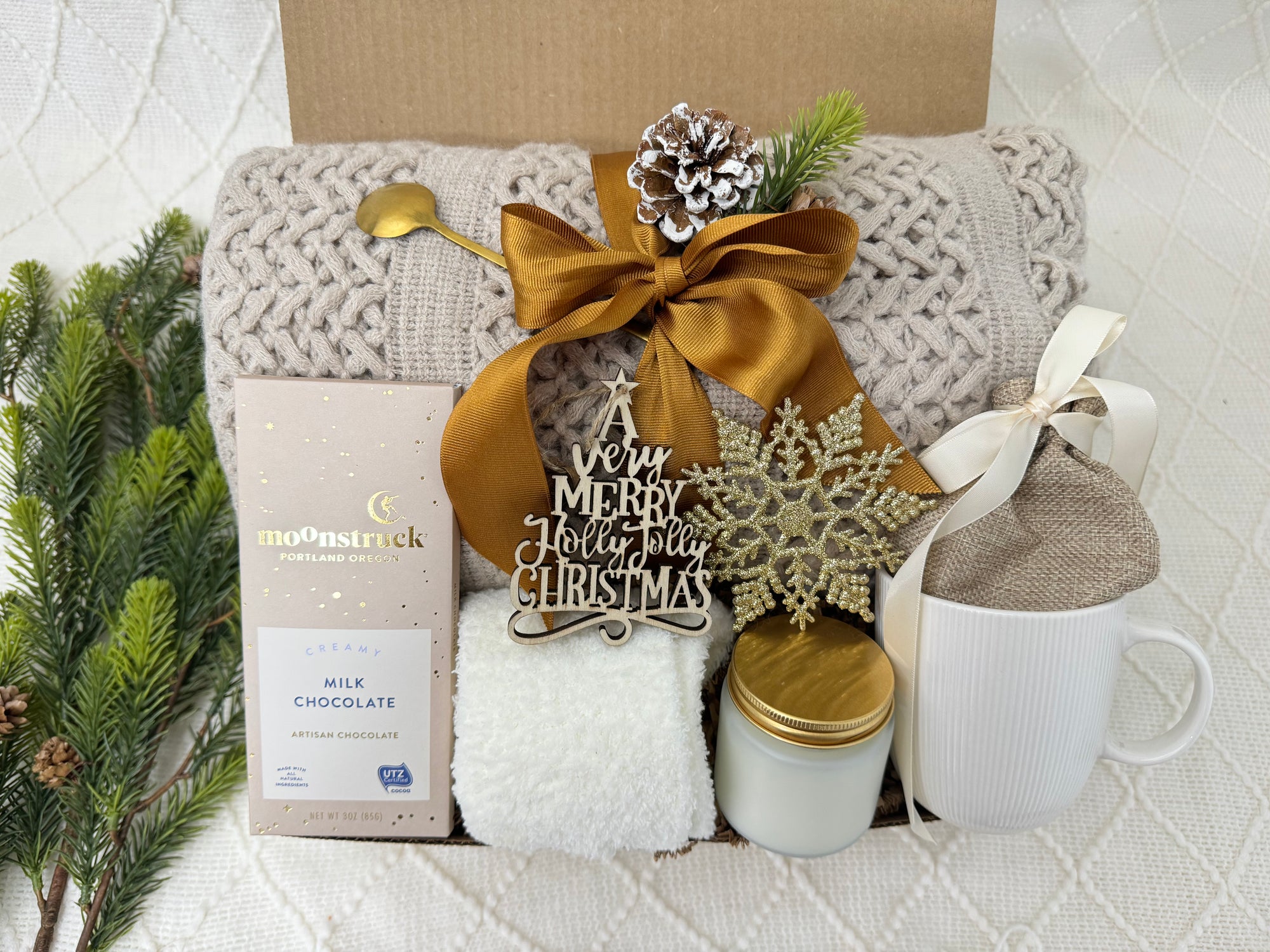 All I Want is You Gift Box by Arinna Gifts featuring a throw blanket, fluffy socks, gourmet chocolate, coffee mug, golden spoon, hot chocolate, candle, and Christmas ornaments.