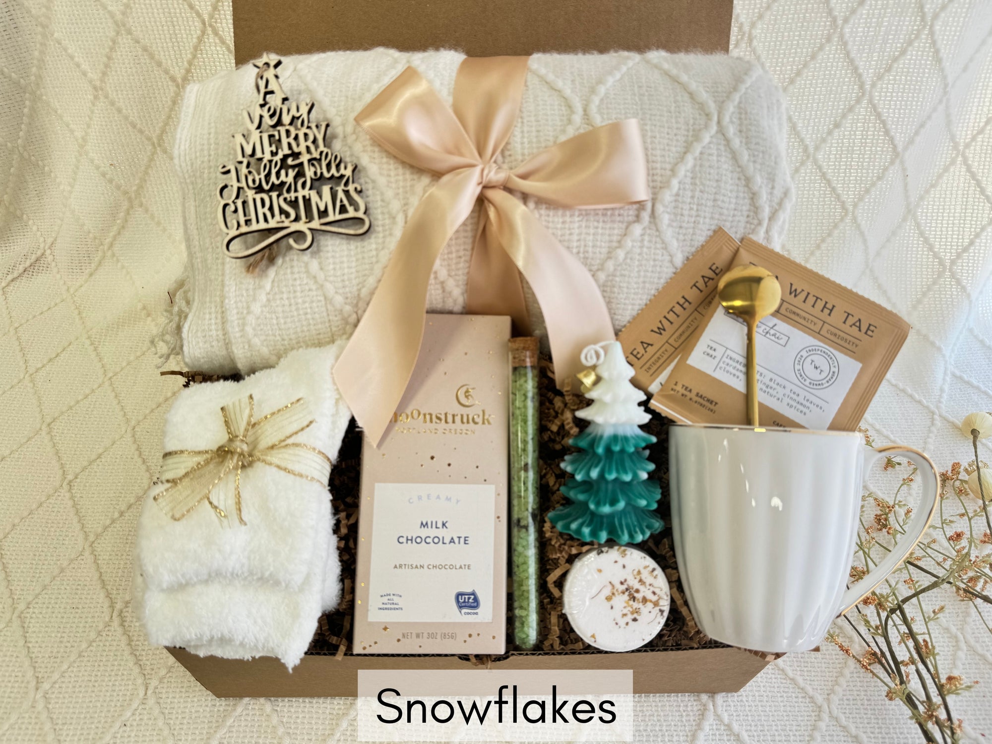 Snowflakes Gift Box by Arinna Gifts featuring a throw blanket, fluffy socks, gourmet chocolate, coffee mug, golden spoon, herbal tea, candle, bath salt, and Christmas ornament.