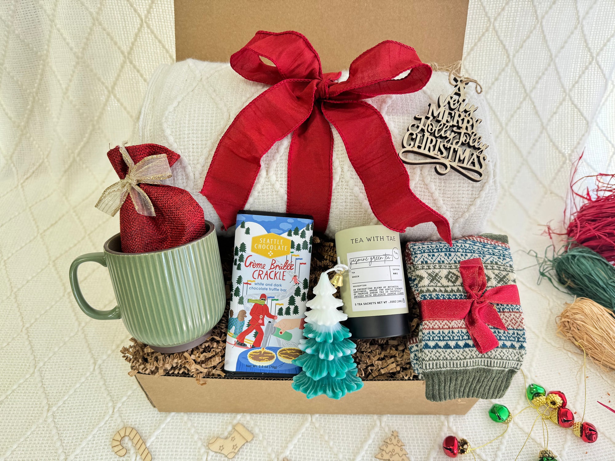 Let’s Stay Home Gift Box by Arinna Gifts featuring a throw blanket, Nordic socks, gourmet chocolate, coffee mug, hot chocolate, candle, herbal tea, and Christmas ornament.