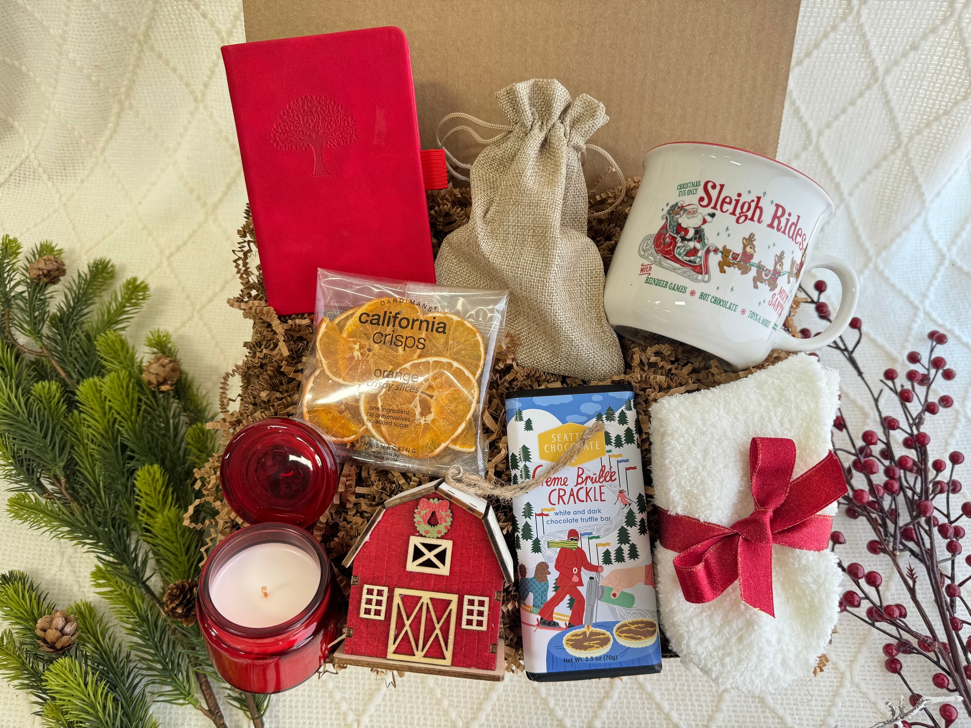 Let It Snow Gift Box by Arinna Gifts featuring a pocket notebook, fluffy socks, gourmet chocolate, coffee mug, hot chocolate, dried orange slices, scent candle, and wooden house ornament.