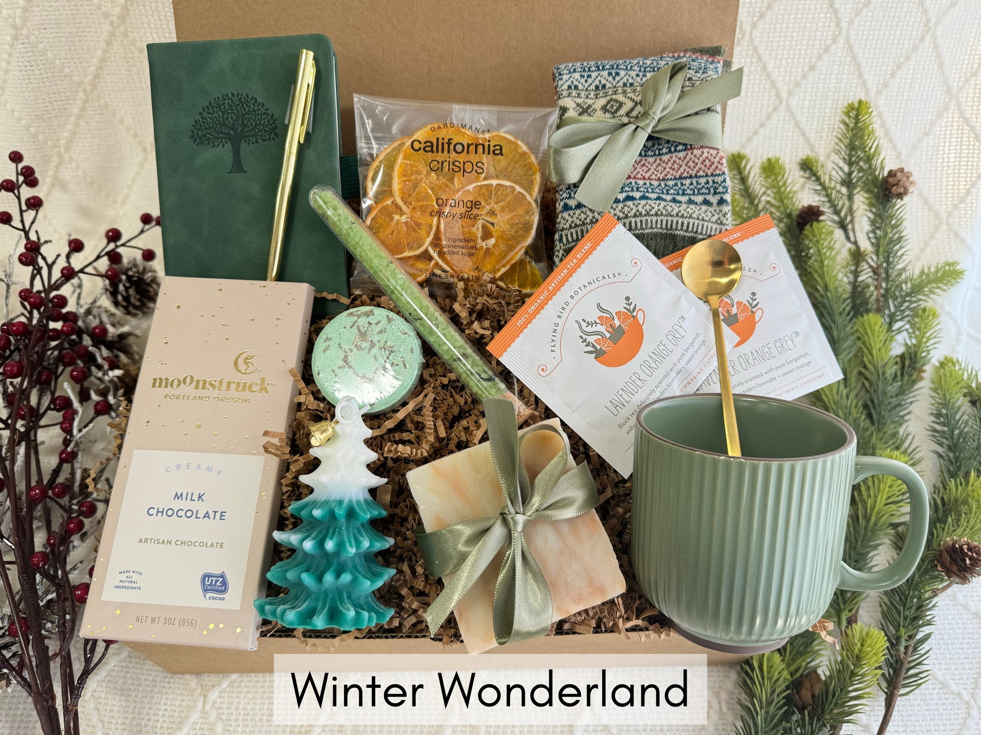 Winter Wonderland Gift Box featuring a pocket notebook, Nordic socks, dried orange slices, coffee mug, gourmet chocolate, herbal tea, handmade soap, bath salt, shower steamer, Christmas tree candle, and golden pen.