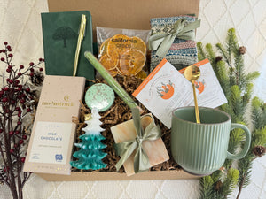 Winter Wonderland Gift Box featuring a pocket notebook, Nordic socks, dried orange slices, coffee mug, gourmet chocolate, herbal tea, handmade soap, bath salt, shower steamer, Christmas tree candle, and golden pen.