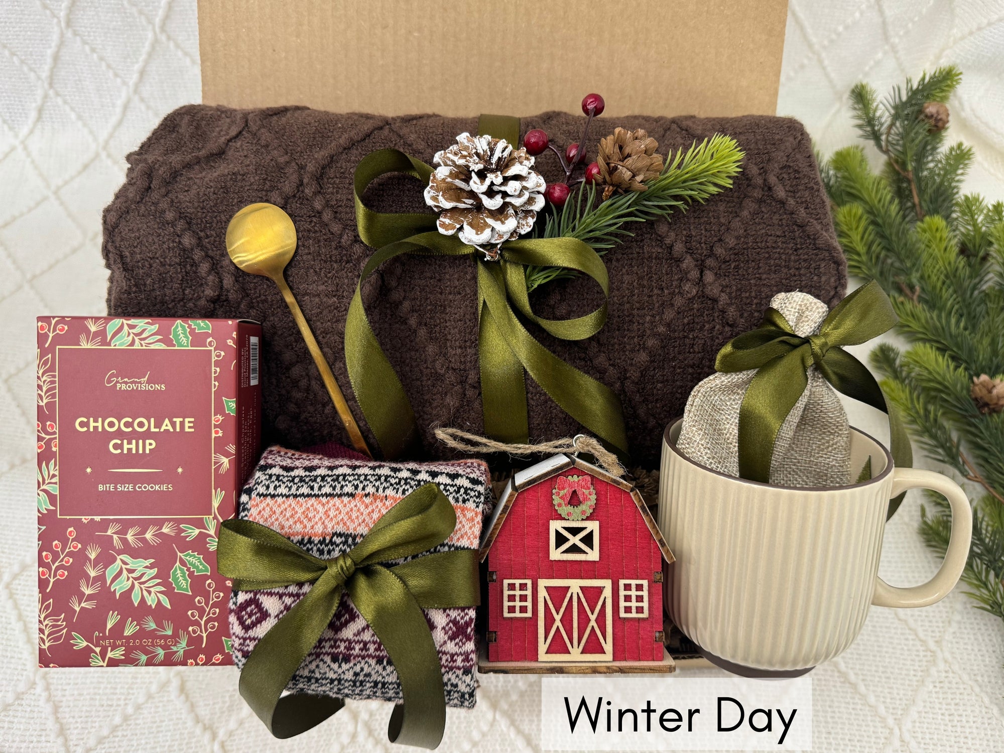 Winter Days Gift Box featuring a throw blanket, Nordic socks, gourmet cookie, coffee mug, golden coffee spoon, wooden house ornament, hot chocolate, and burlap bag.