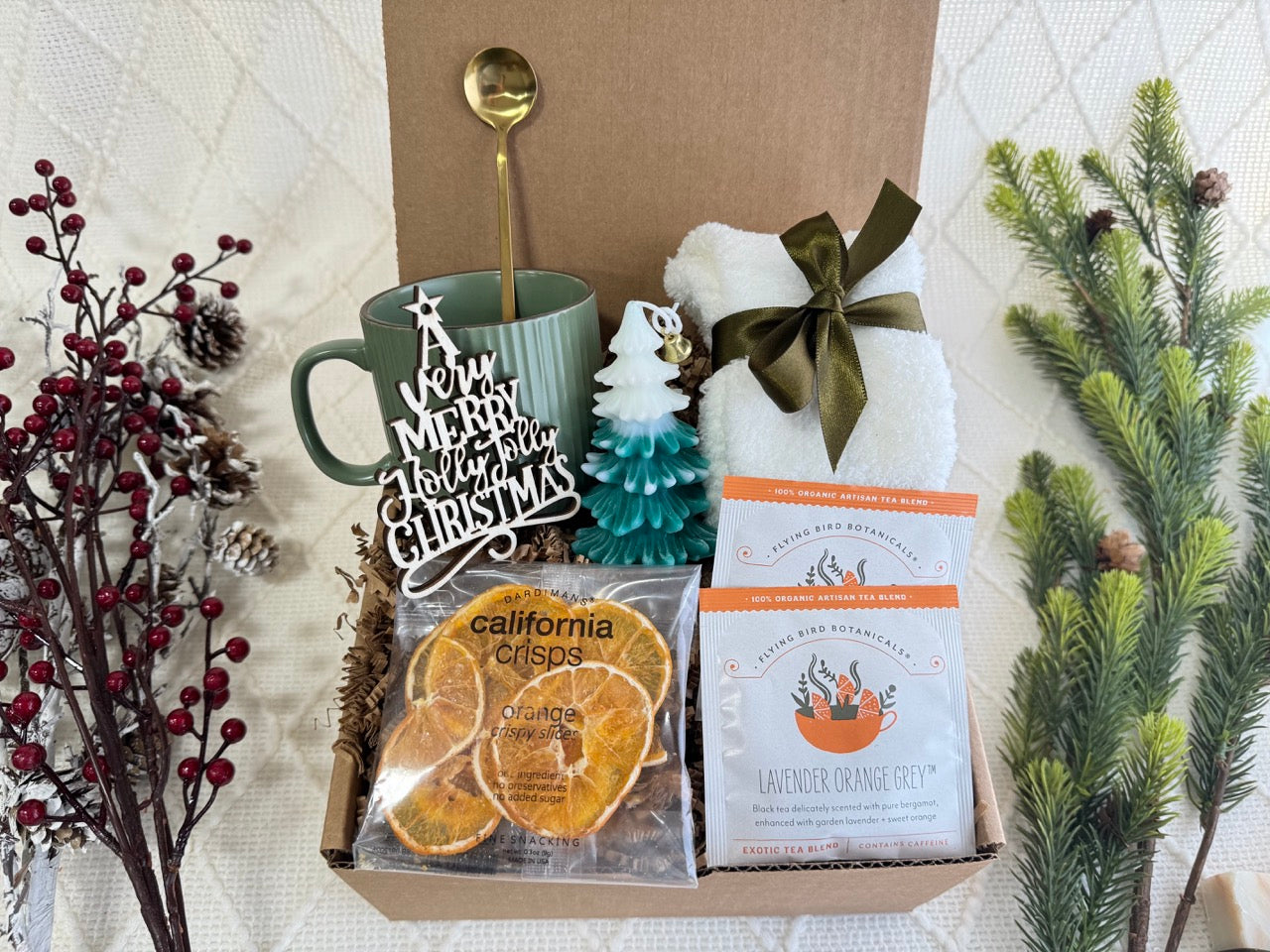 O Christmas Tree Gift Box featuring white fluffy socks, coffee mug, golden coffee spoon, dried orange slices, herbal tea, Christmas tree candle, and wooden Christmas ornament.