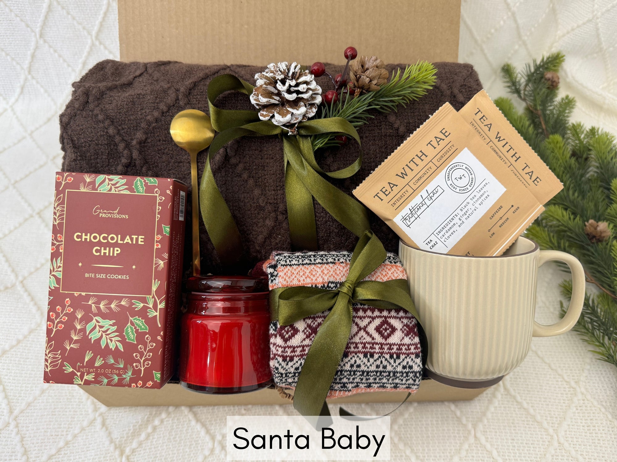 Santa Baby Gift Box featuring a throw blanket, Nordic socks, gourmet cookie, coffee mug, golden coffee spoon, herbal tea, and a scent candle.