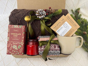 Santa Baby Gift Box featuring a throw blanket, Nordic socks, gourmet cookie, coffee mug, golden coffee spoon, herbal tea, and a scent candle.