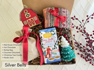 Silver Bells Gift Box featuring Nordic socks, gourmet chocolate, Christmas tree candle, hot chocolate, burlap bag, and wooden house ornament.