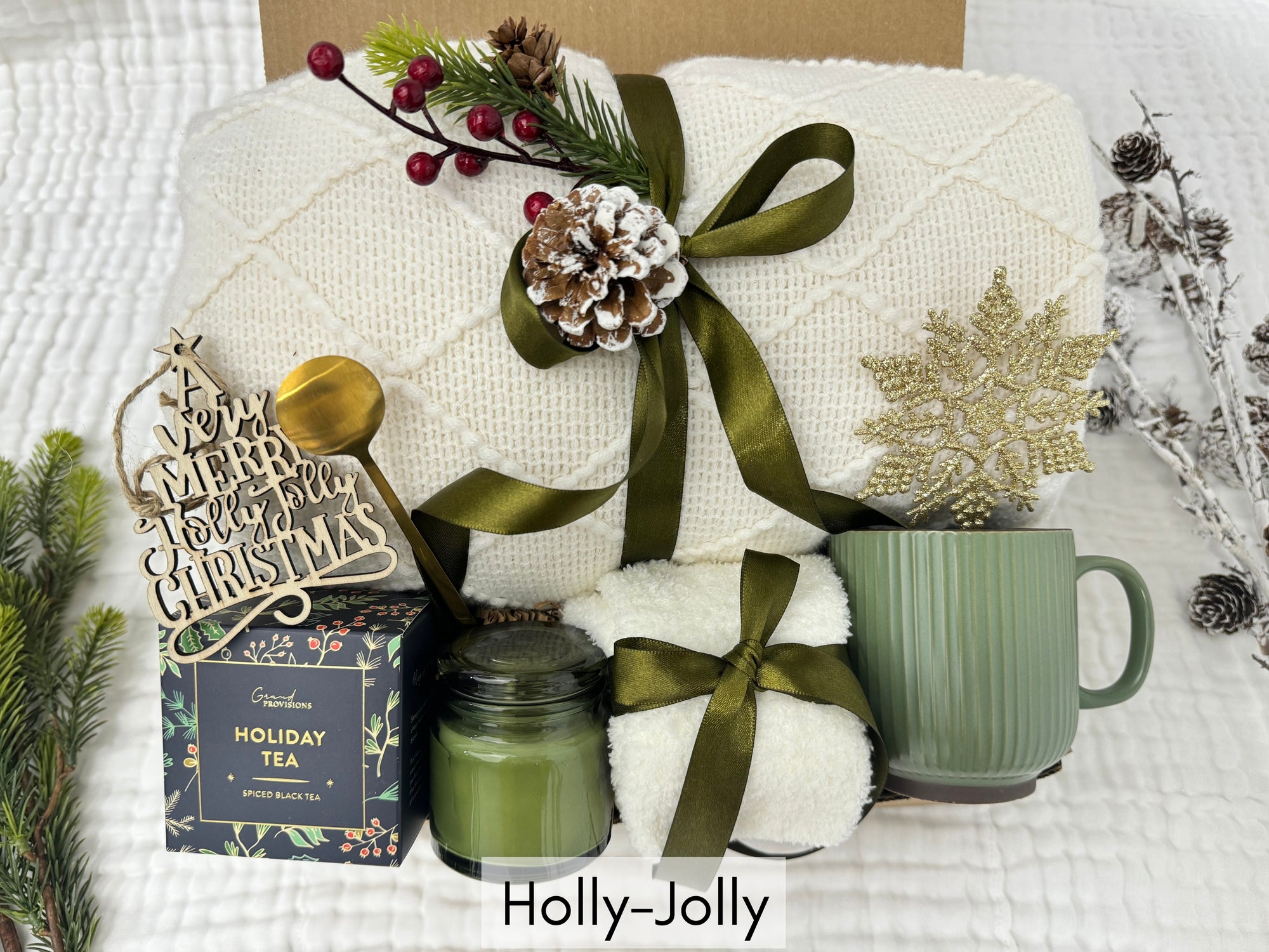 Holly-Jolly Gift Box featuring a throw blanket, fluffy socks, scent candle, coffee mug, golden coffee spoon, snowflake Christmas ornament, holiday tea, and wooden Christmas ornament.