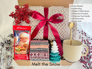 Melt the Snow Gift Box featuring a throw blanket, Nordic socks, hot chocolate, Christmas tree candle, coffee mug, golden coffee spoon, and snowflake Christmas ornament.