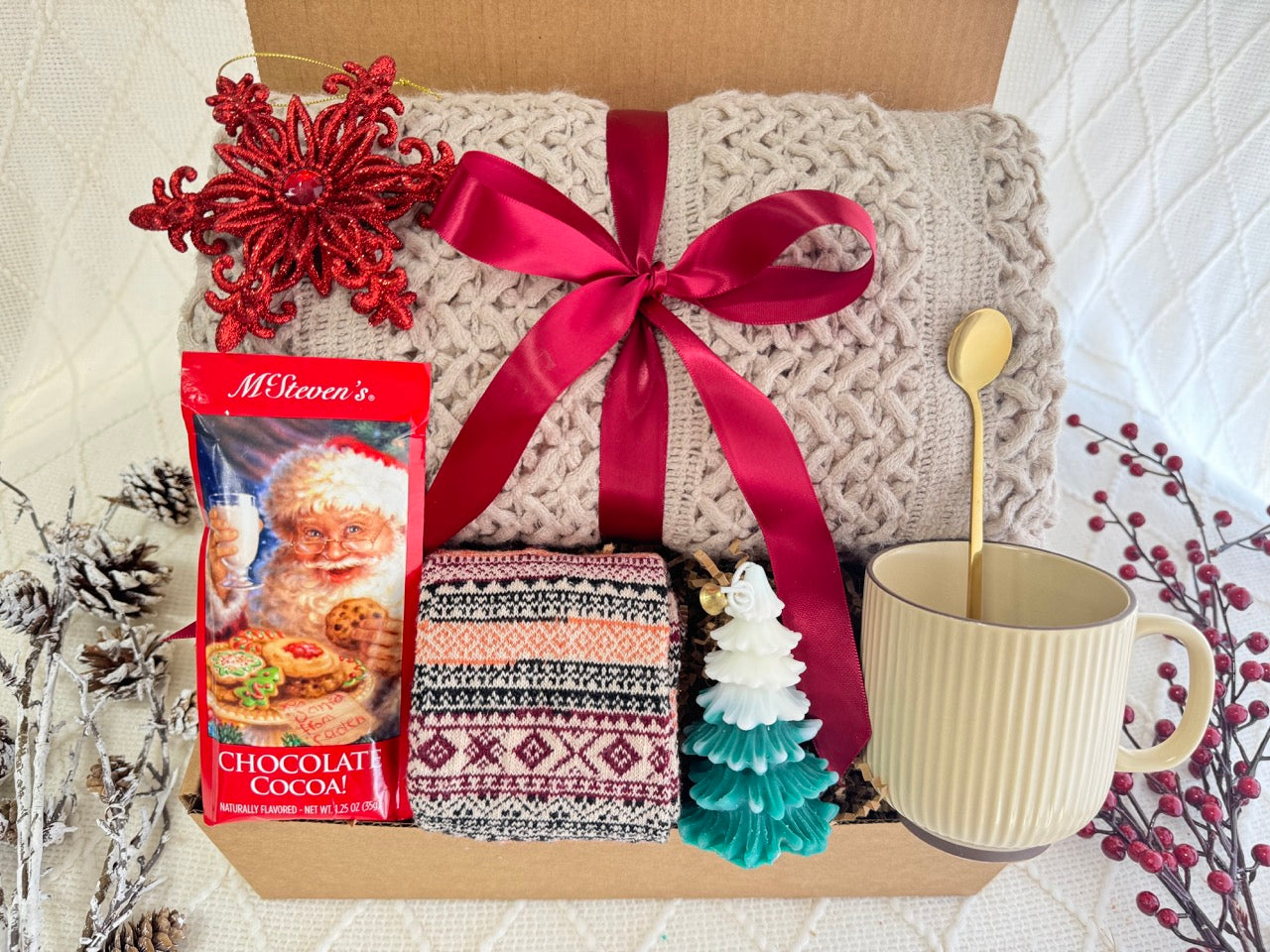 Melt the Snow Gift Box featuring a throw blanket, Nordic socks, hot chocolate, Christmas tree candle, coffee mug, golden coffee spoon, and snowflake Christmas ornament.