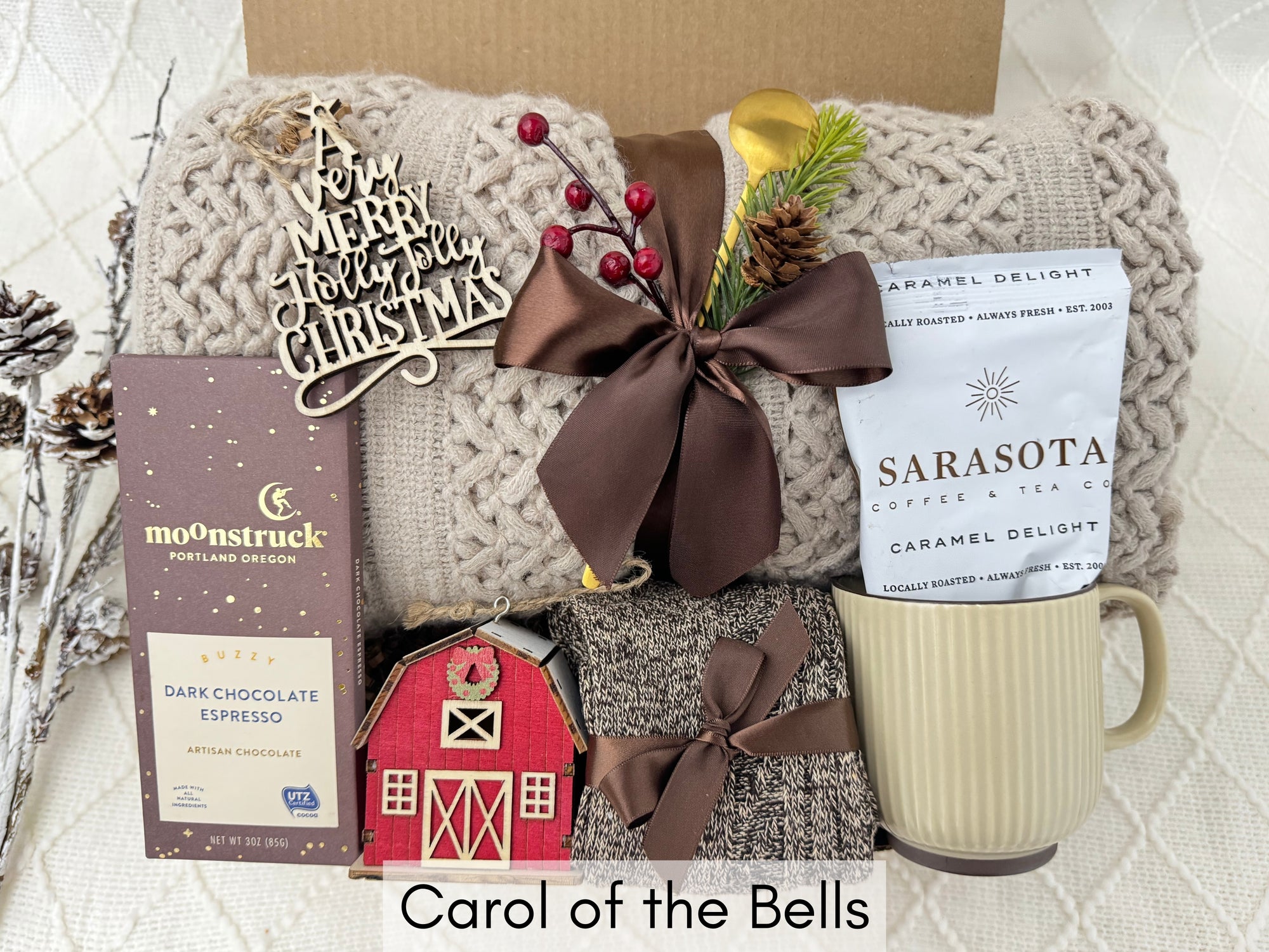 Carol of the Bells Gift Box featuring a throw blanket, Nordic socks, wooden house ornament, wooden Christmas ornament, coffee mug, golden coffee spoon, and ground coffee.