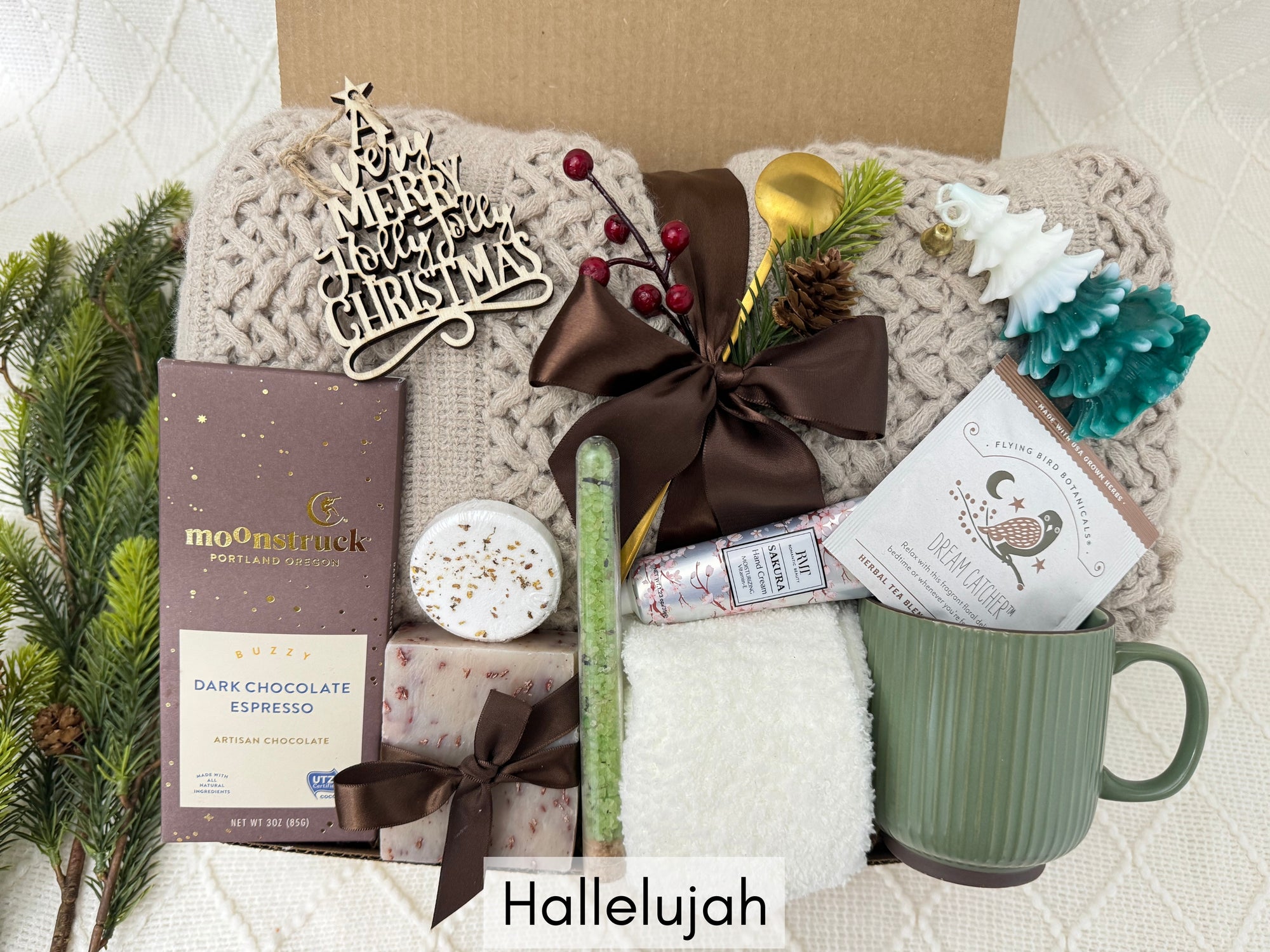 Hallelujah Gift Box featuring a throw blanket, white fluffy socks, wooden Christmas ornament, handmade soap, bath salt, shower steamer, hand cream, coffee mug, golden coffee spoon, herbal tea, Christmas tree candle, and gourmet chocolate.